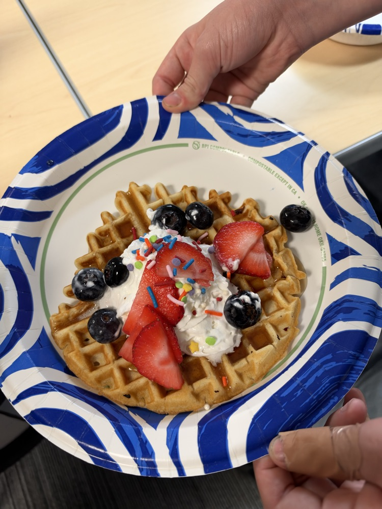 a plate with a waffle with syrup whipped cream and strawberry 