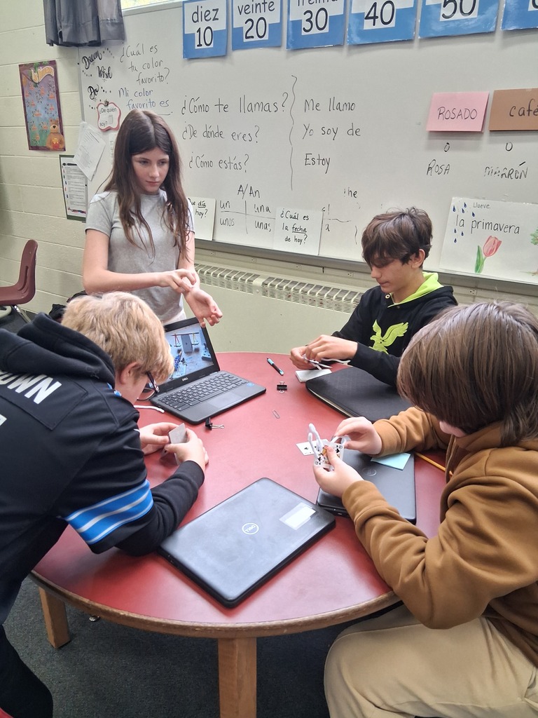 students work at a round table with one Chromebook open while creating a project with cards