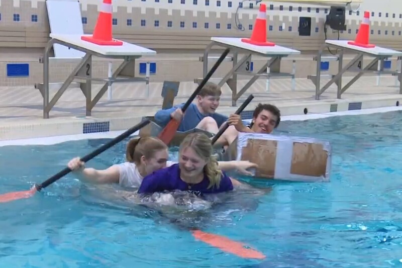 Students in cardboard boats in pool racing 