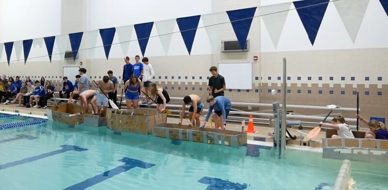 Students in cardboard boats in pool racing 