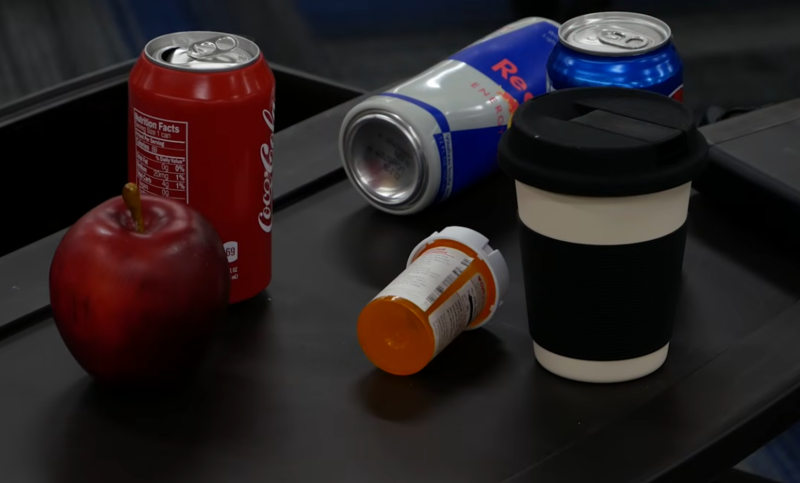 Photo of an apple, a coke can, a red bull can, some prescription drugs in a plastic jar and a coffee-like cup