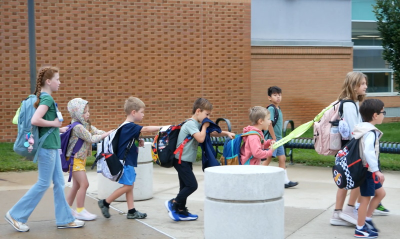 photo of two girls leading young boys near the curb by school busses