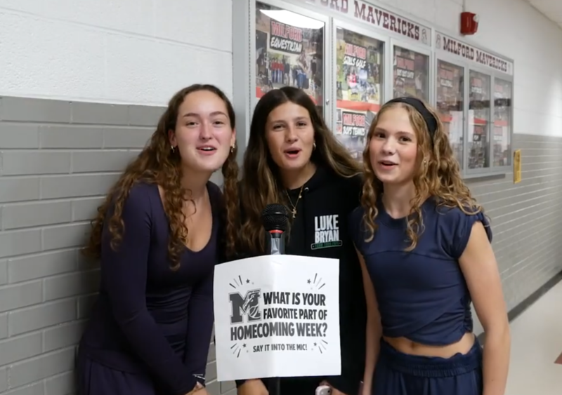 Several girls standing in front of a microphone that reads "what's your favorite part of homecoming week?" written on the mic stand