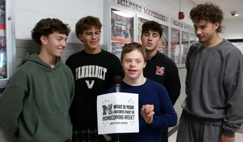 Several boys standing in front of a microphone that reads "what's your favorite part of homecoming week?" written on the mic stand