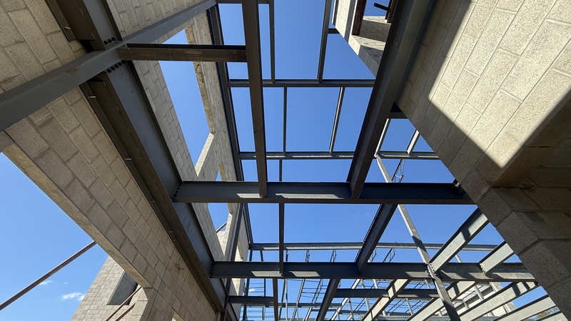 Photo of girders on top of a construction site building.. looking up into the blue sky man in a hard hat walking on a construction site with cinder block walls up