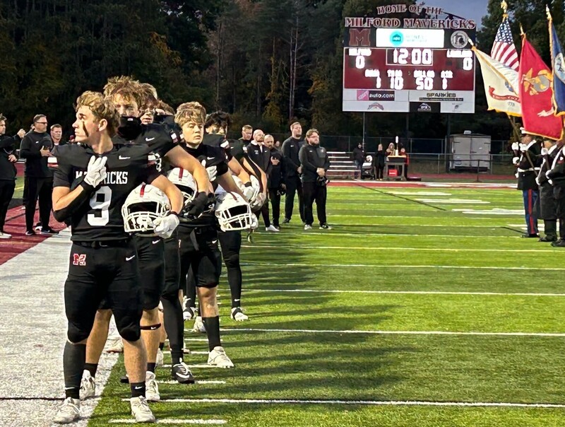 Football players lined up on the sideline of a football field with hands over hearts
