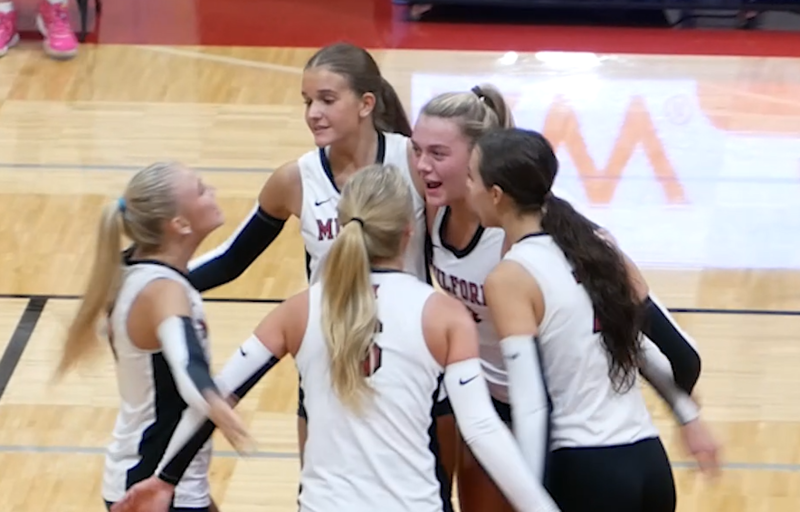 Photo of 5 volleyball players hugging on the court during a match