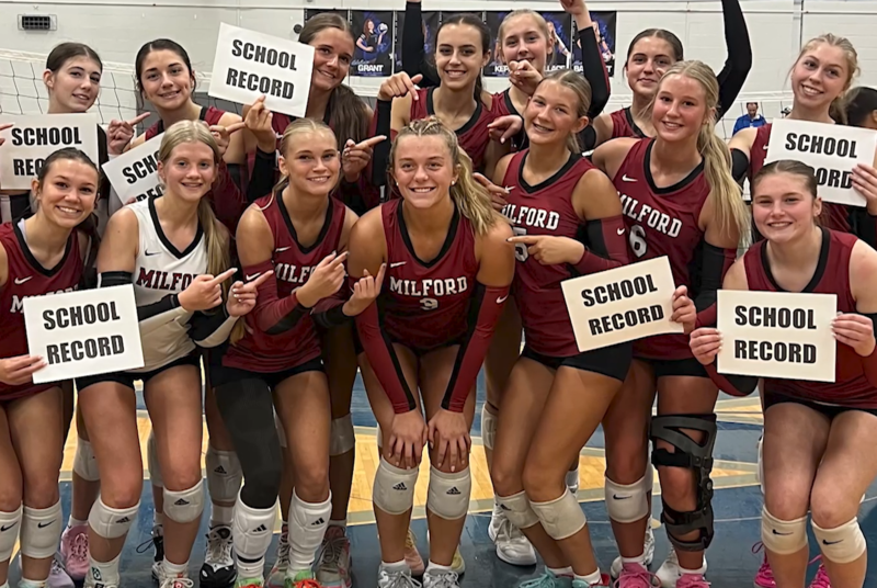 Team photo with several volleyball girls posing for a photo holding signs that read "school record"