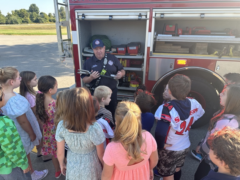 Firefighter explaining tools on a firetruck to students