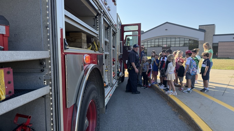 Students looking inside a firetruck and firefighter explaining what they see.