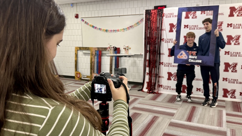 Girl takes photo of two boy wearing hope college gear and holding a hope college sign 