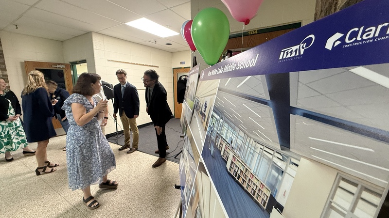 Photo of people standing in background with renderings and balloons in the foreground