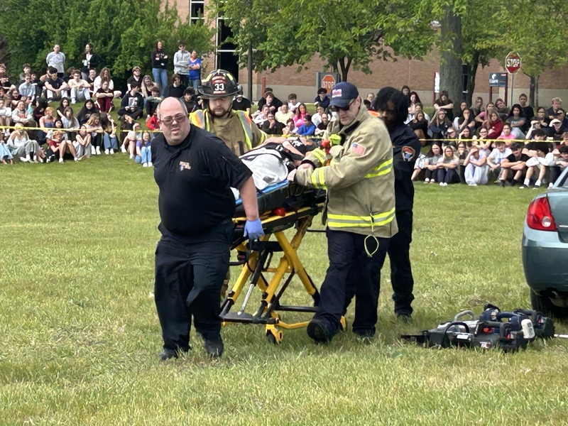 emergency workers lifting student in gurney during mock car crash simulation