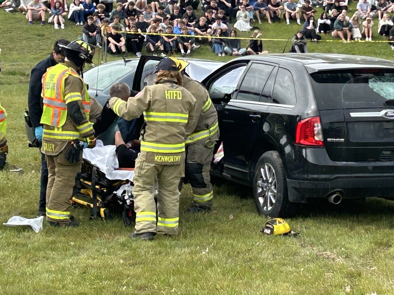emergency workers lifting student during mock car crash simulation