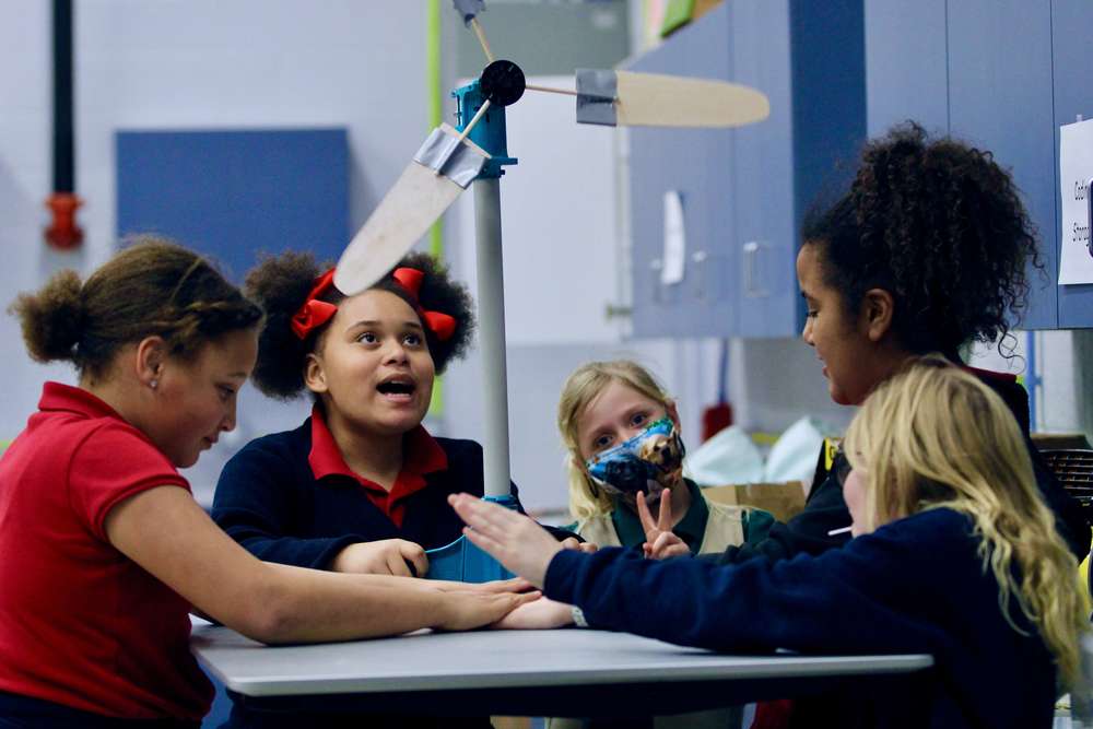five school age girls sit around a wind mill during kid wind practice