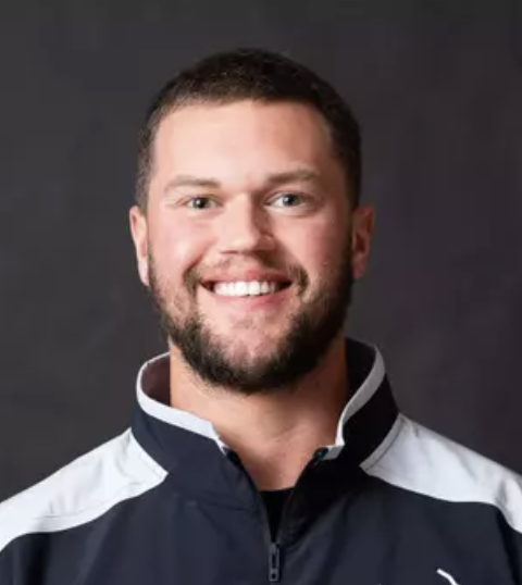 Headshot of Luke Berblinger. A Caucasian Man with short dark hair, wearing a black and white collared shirt smiles for the camera.