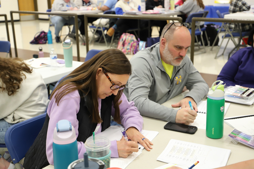 a woman in a purple and black shirt is writing in a book.