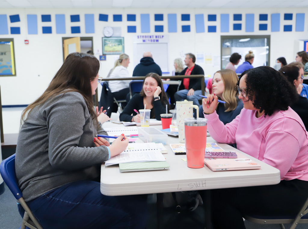 people are sitting at a table with workbooks and cups