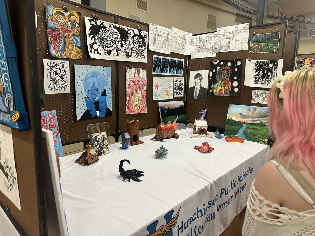 a woman standing in front of an art display with ceramics on the table and art hanging on the wall.