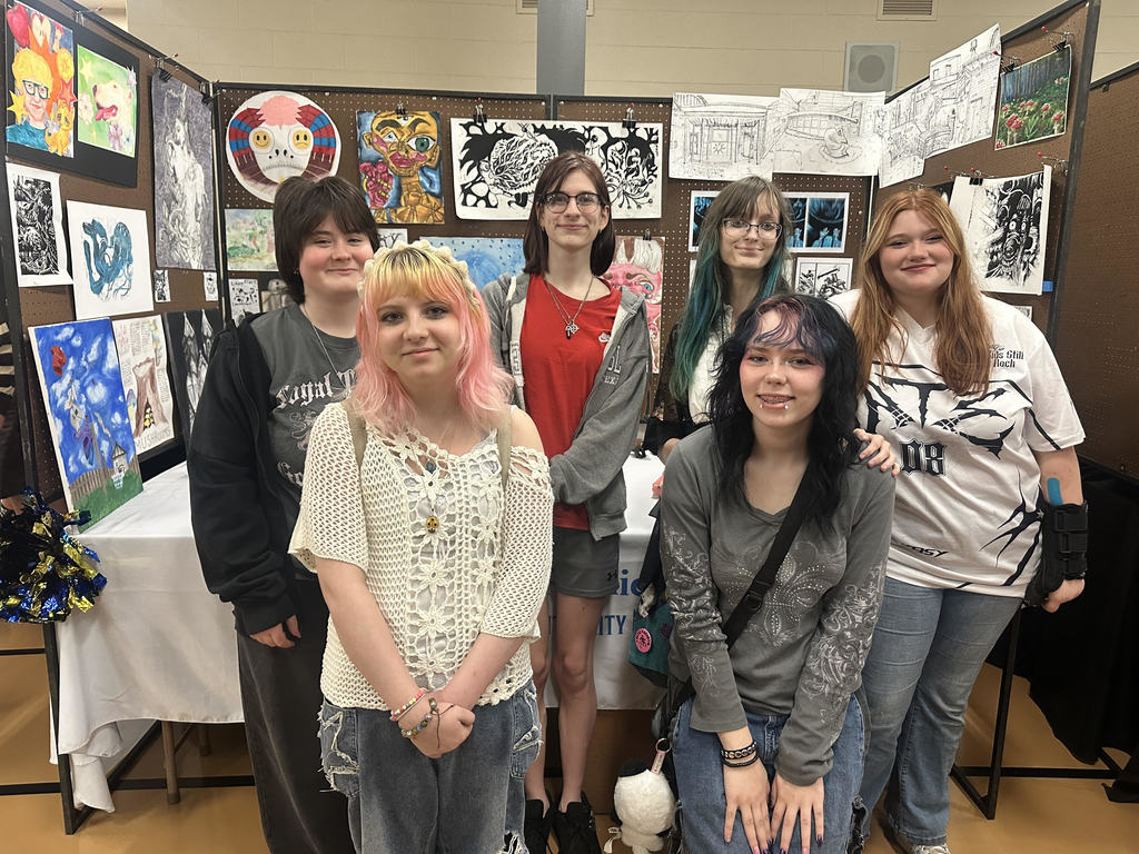 students stand in two rows in front of art display shown behind them