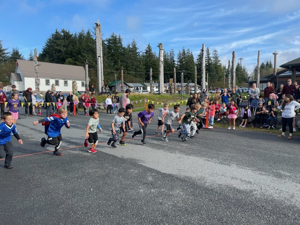 ChatGPT said: Young runners burst off the starting line at Hydaburg School’s home cross country meet, cheered on by classmates, families, and community members during the K–2 boys’ race.