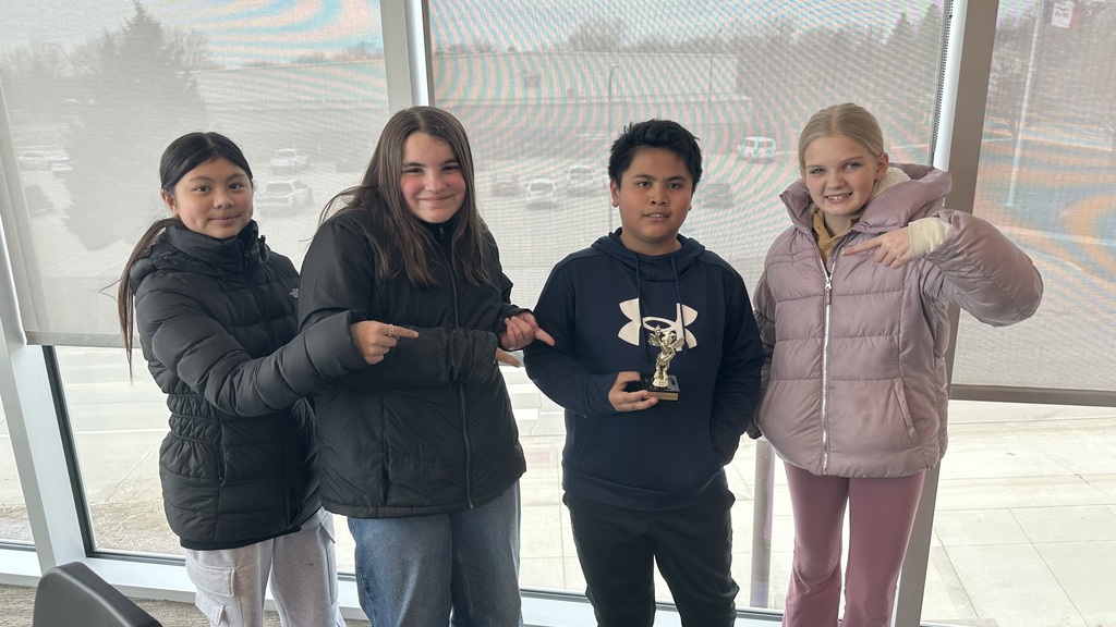 three girls pointing to trophy of a boy holding it.