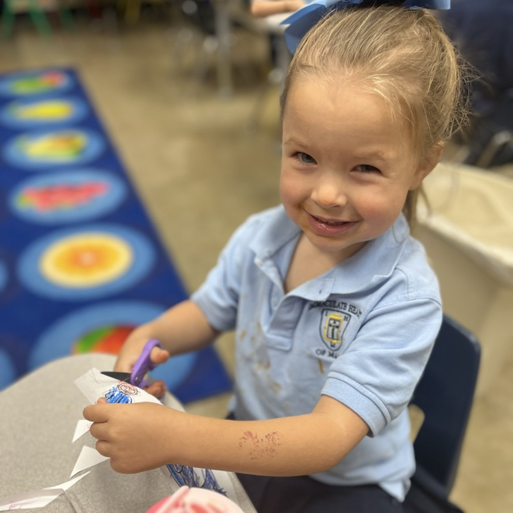 a student smiling at the camera and cutting a whale they colored.
