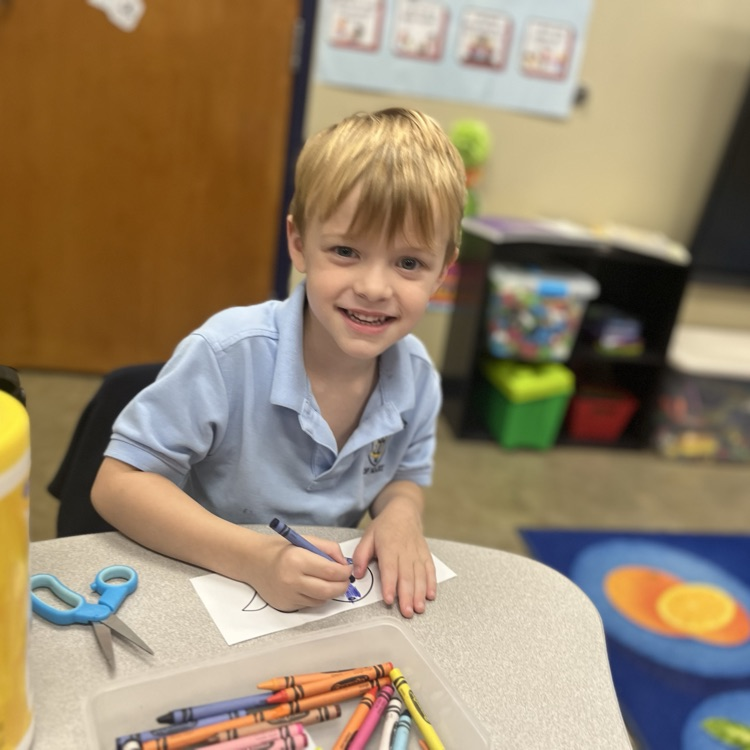 a student smiling at the camera and coloring a whale craft