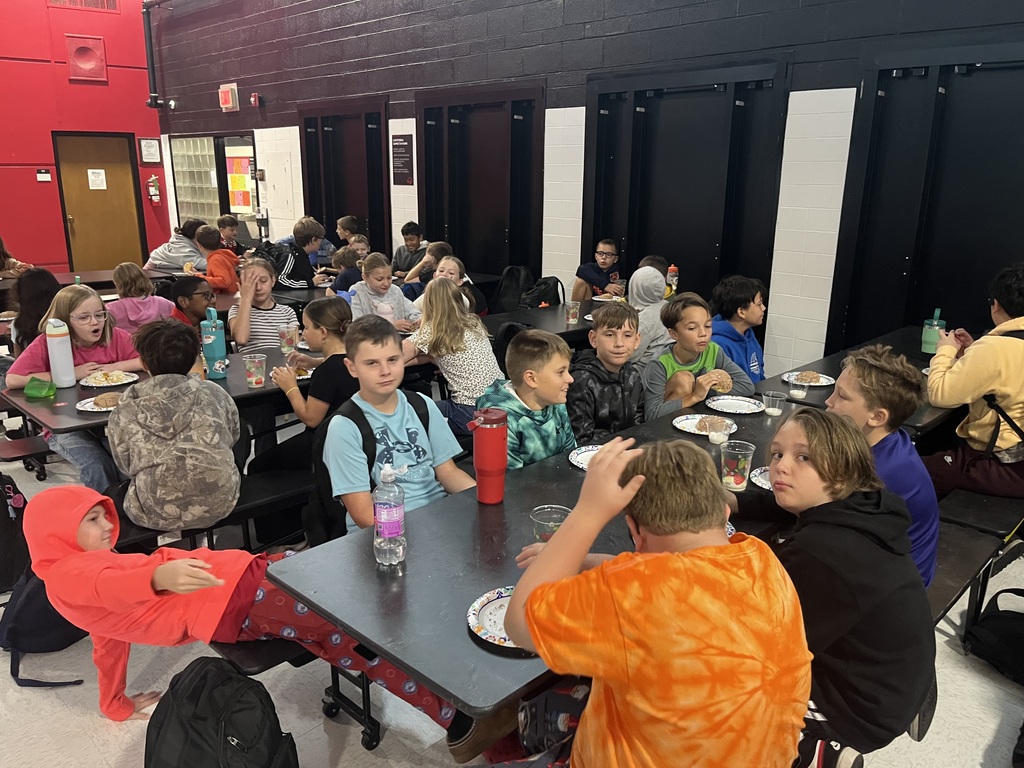 A cafeteria filled with students sitting at tables, eating food. The room has red and black walls.