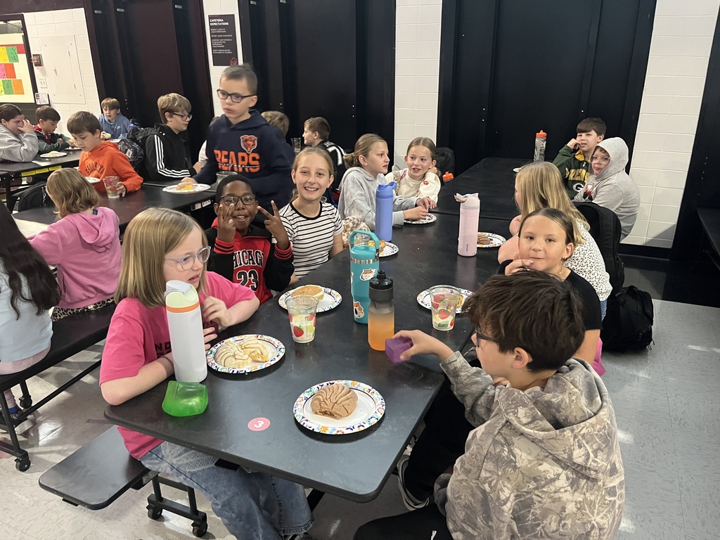 Students seated at a table, enjoying a meal. Plates, cups, and food items are on the table.