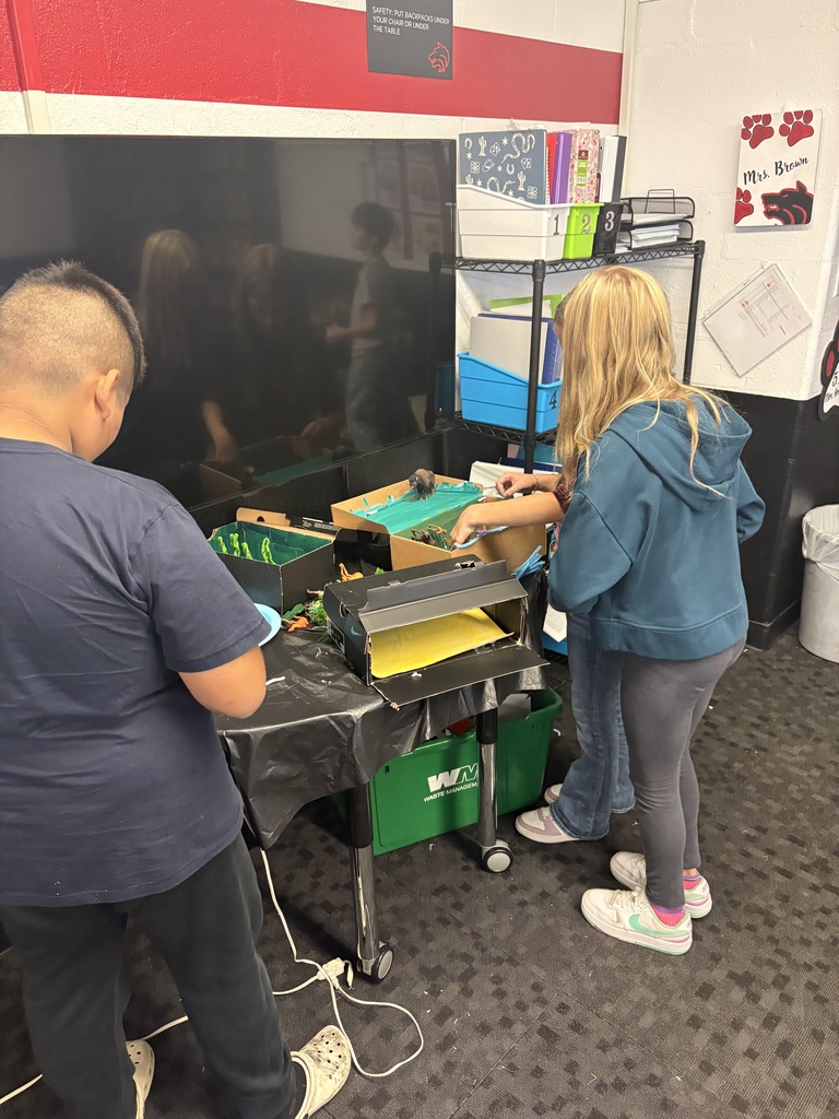 Two people working together on a project. One person stands and one bends. Behind them is a large screen.