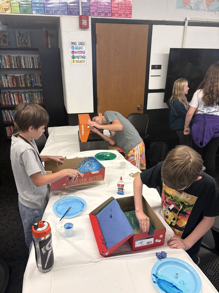 Kids painting inside a cardboard box on a table. 