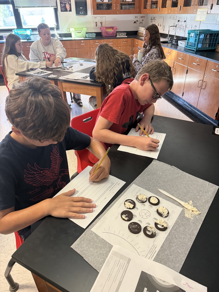 Two boys working at a lab table, each with papers and writing utensils, in a science classroom.