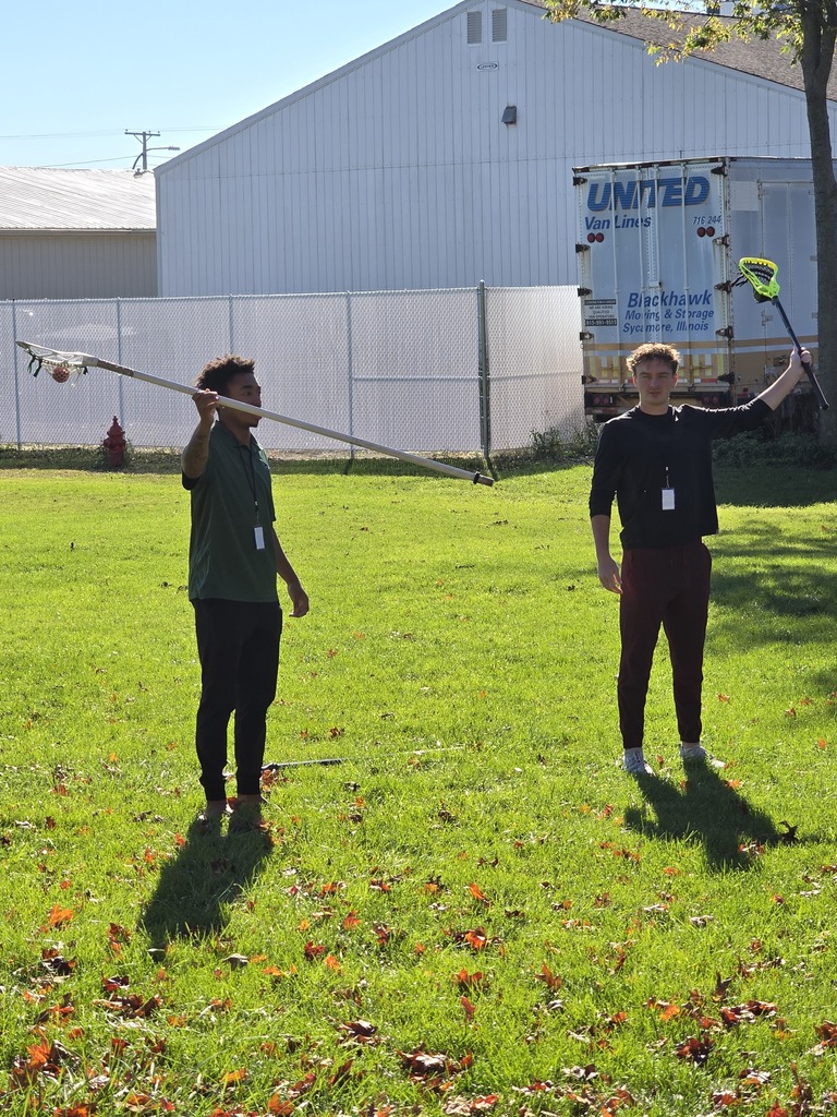 Two people standing on grassy field holding  lacrosse sticks