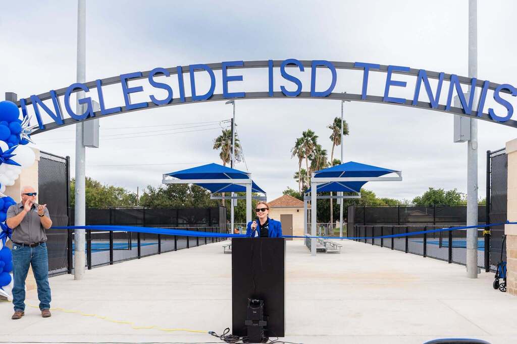 People standing at a podium on a tennis court. Archway overhead reads "SINGLESIDE ISD TENNIS".
