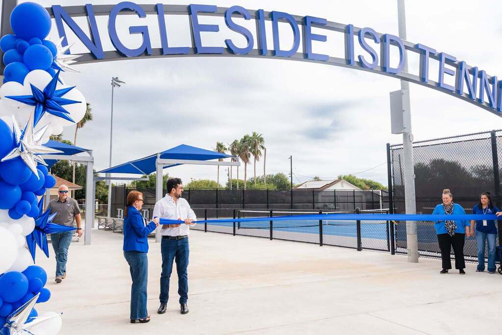 Group of people standing at the entrance of a tennis court. One person holds a ribbon.