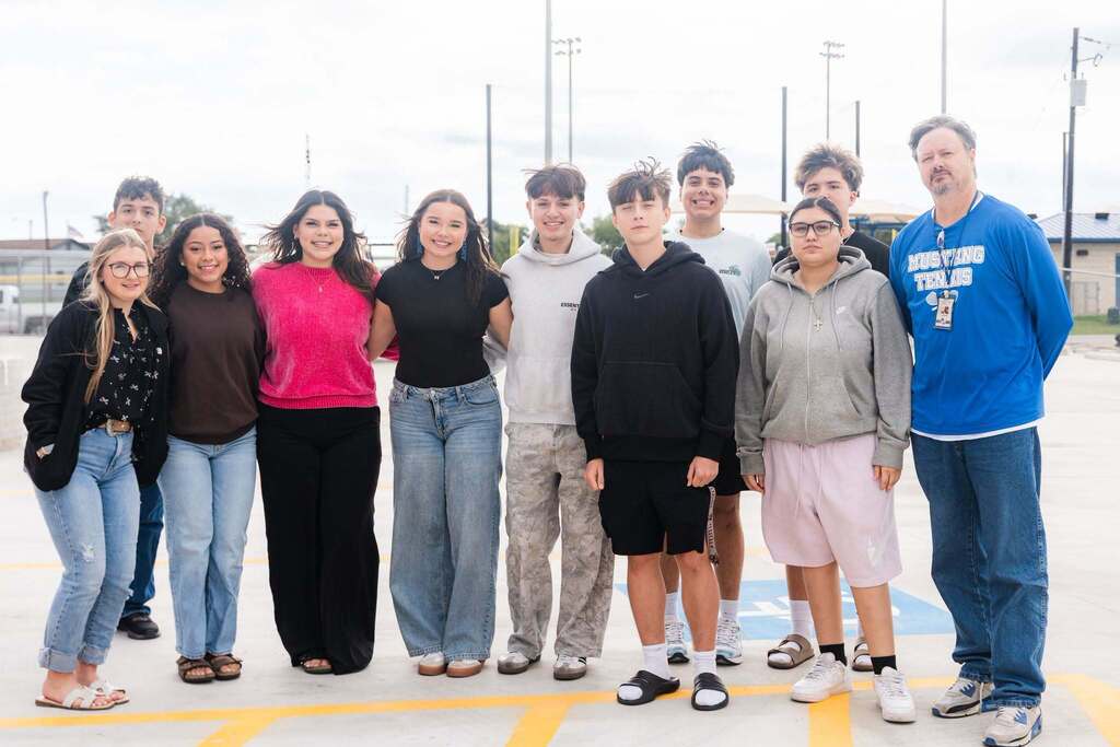 Students and adults in a parking lot pose for a group photo. They stand next to each other, some wearing sneakers.