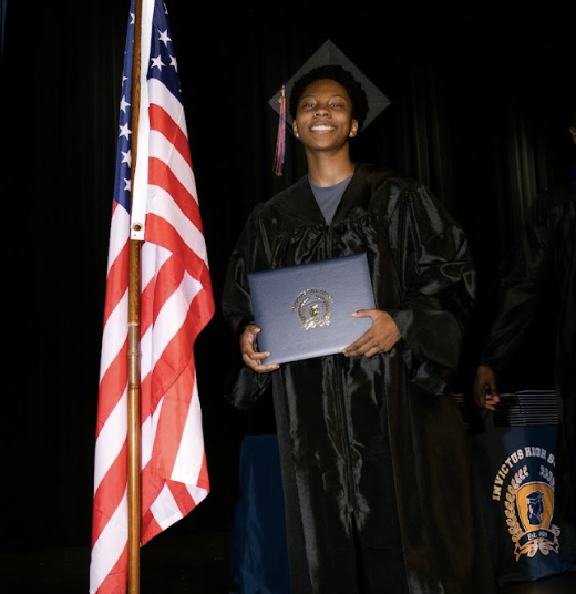 A smiling graduate holds up their diploma
