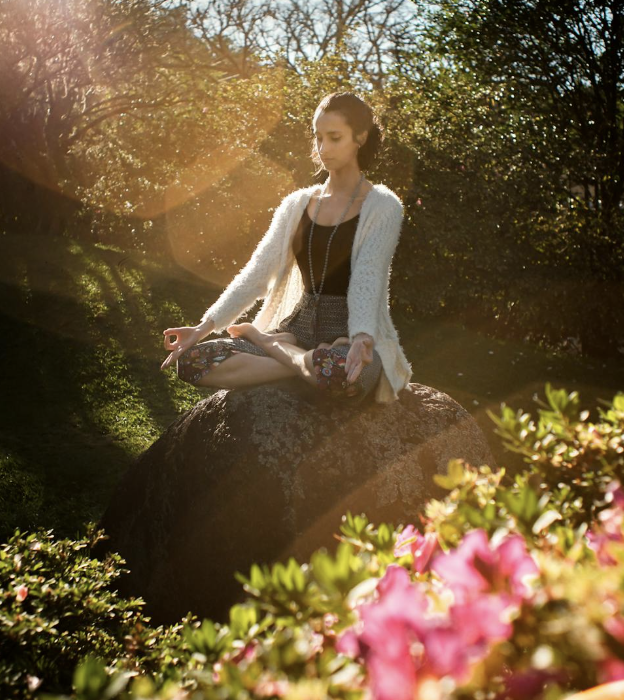 A young woman sits on a large rock meditating