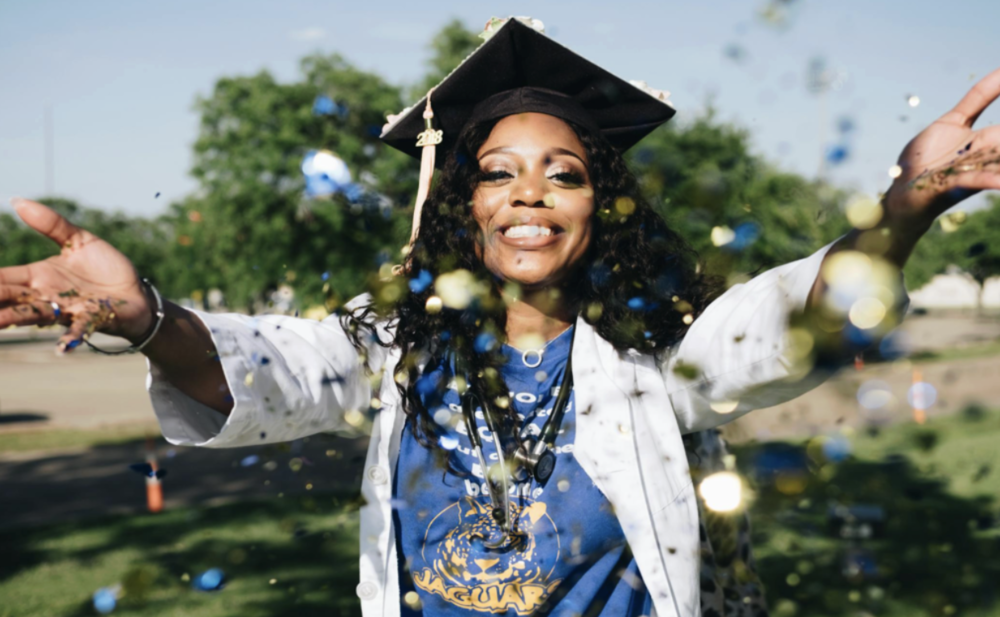 A smiling graduate tosses confetti.