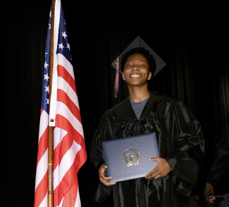 A smiling graduate holds up their diploma
