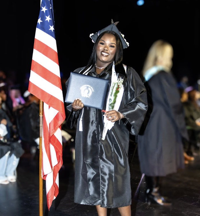 A graduate smiles and shows her diploma on stage at graduation.
