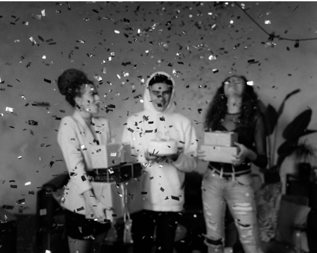 A group of people stand with boxes surrounded by celebratory confetti