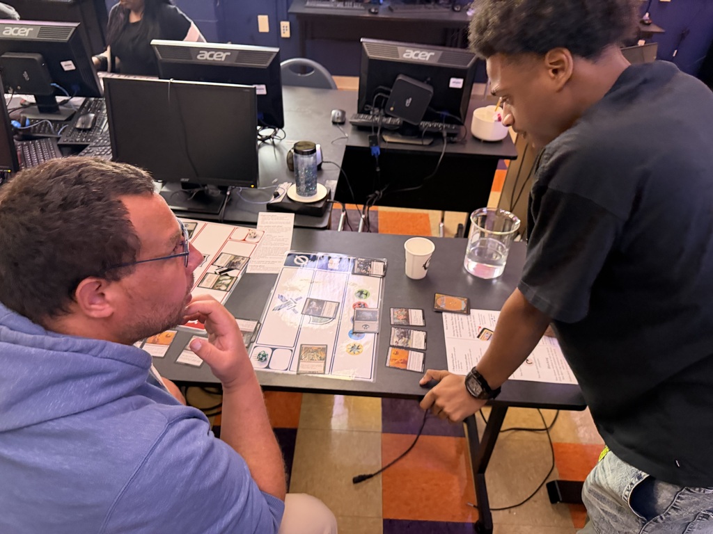 A teacher and student strategize over Magic cards
