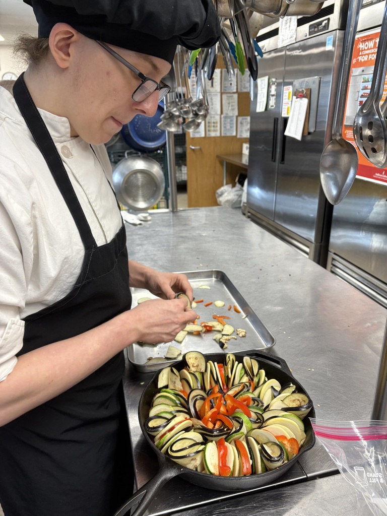 student preparing skillet of ratatouille