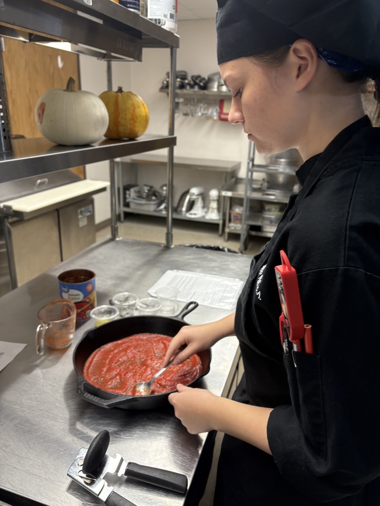 student stirring skillet of tomato sauce