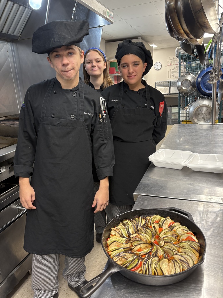 three student standing by a skillet of ratatouille