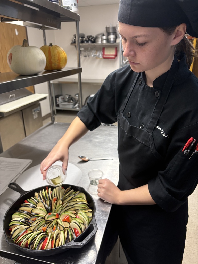 student adding oil to skillet of rataouille