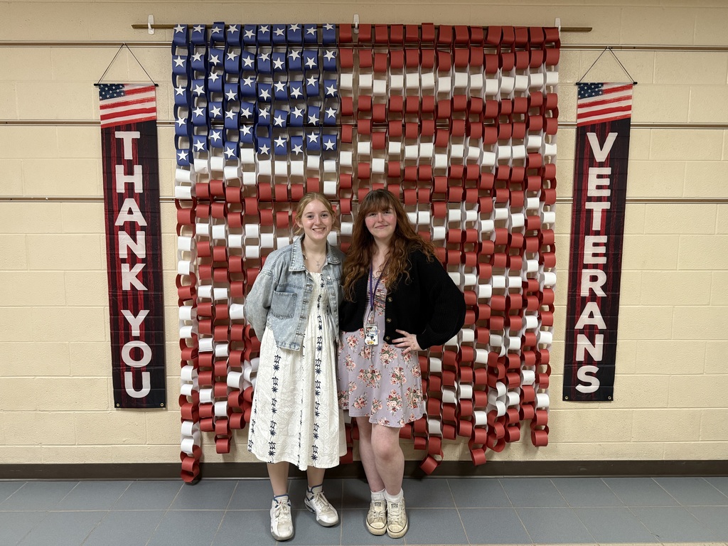 two girls standing in front of paper chain American flag with Thank You Veterans signs on the sides of it