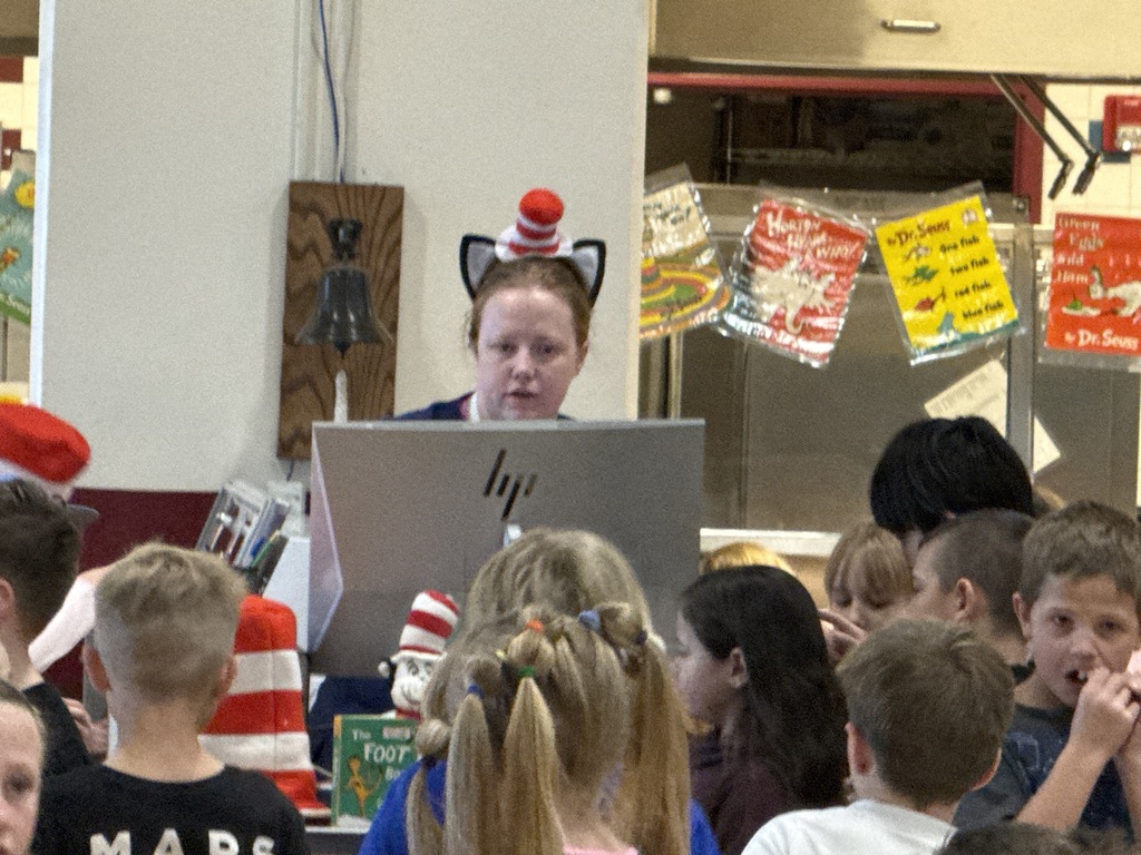A lunch aide wears a  cat in the hat headband as she checks students in. 